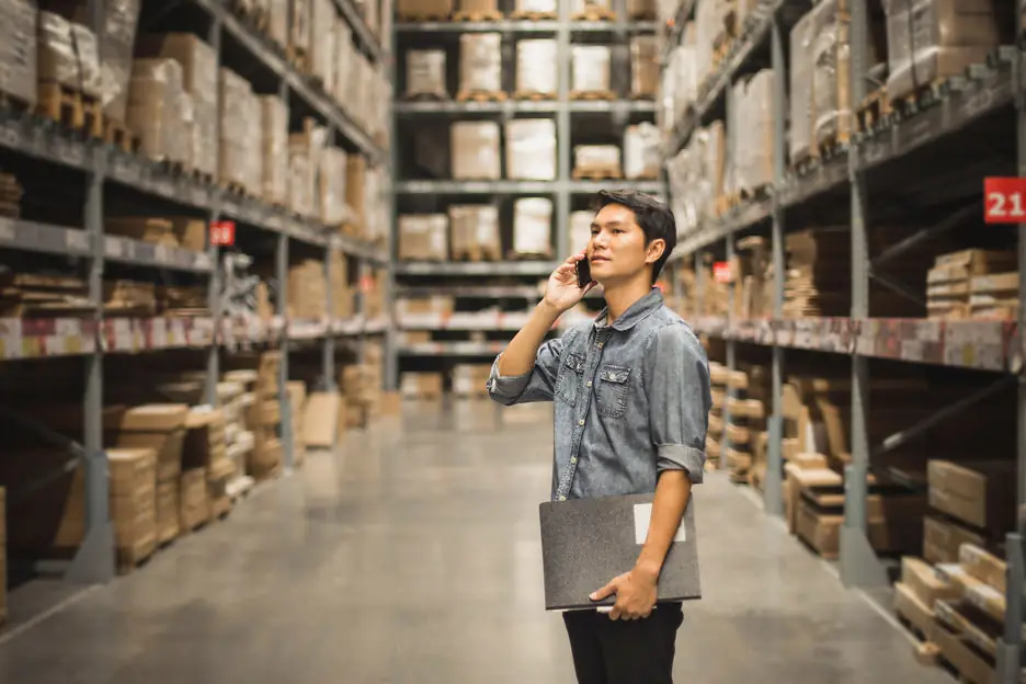 An owner on the phone in his stockroom, laptop under his arm.
