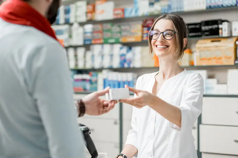A pharmacist handing a customer their purchase across the counter: the day's card sales.