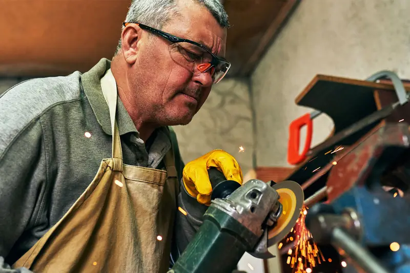A metalworker at the grinder in safety glasses, with the machine the work depends on.