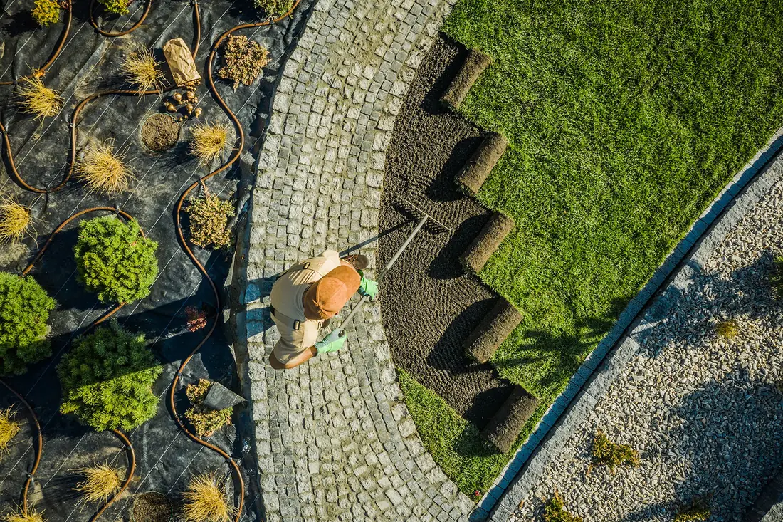 A landscaper laying stone beside new turf, seen from above: work that shows.