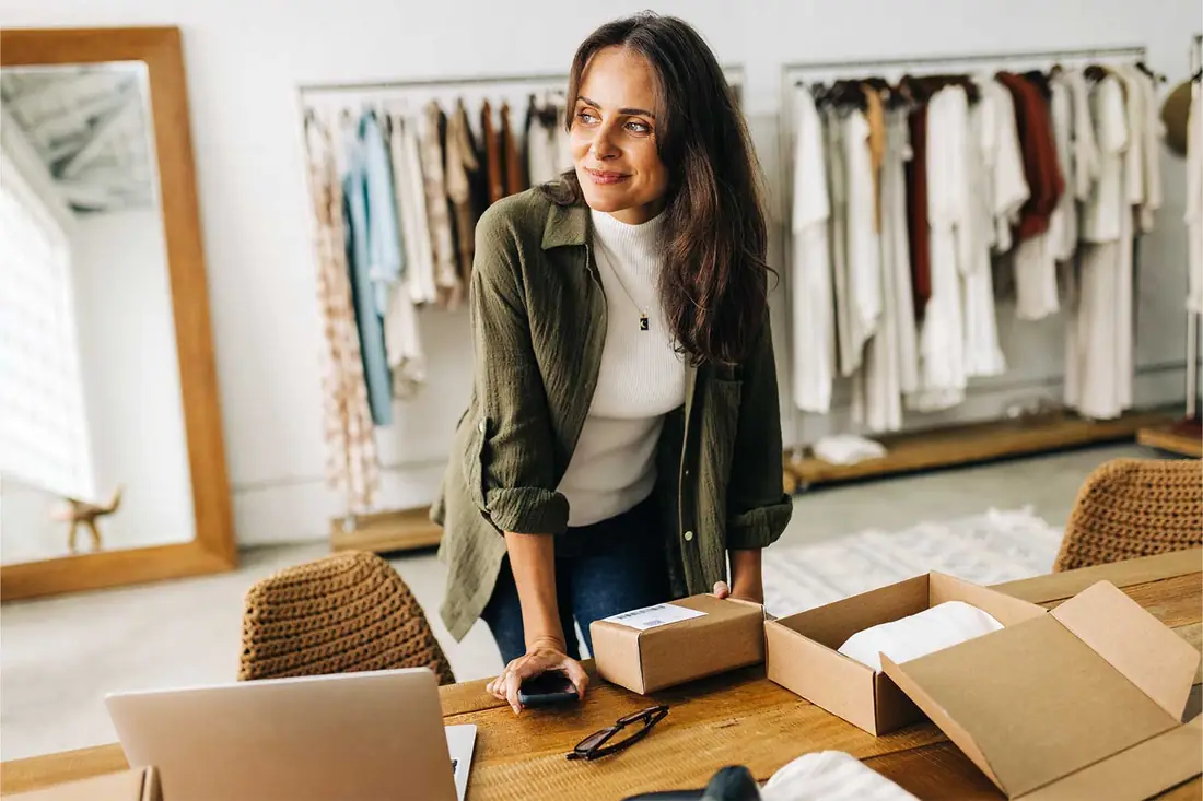 An online seller at her desk between orders, boxes packed and laptop open.