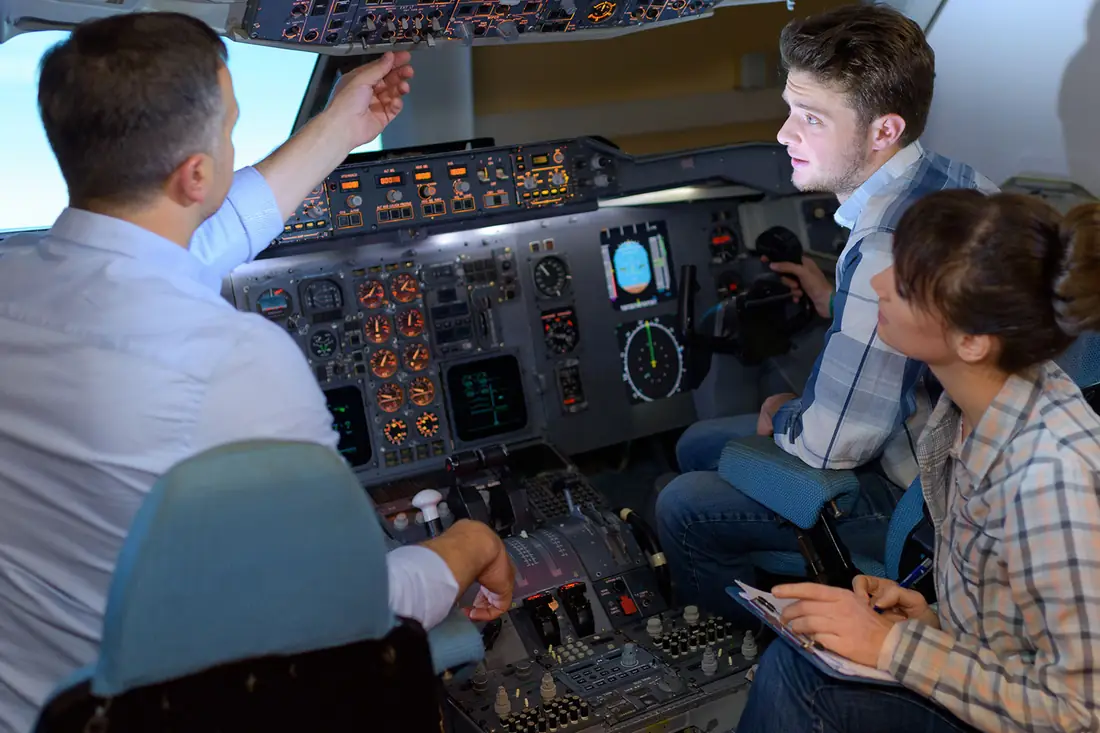 A flight-school instructor and two trainees reading a simulator's instruments together.